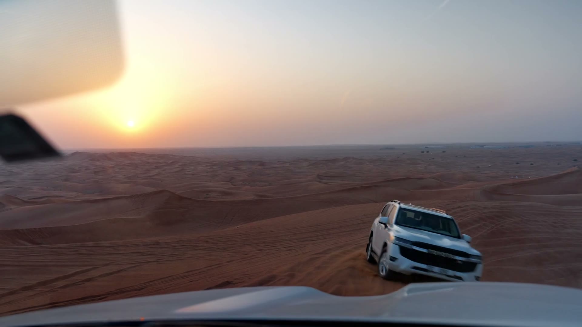 A white 4x4 on a dune at sunset, seen over the bonnet of the car ahead