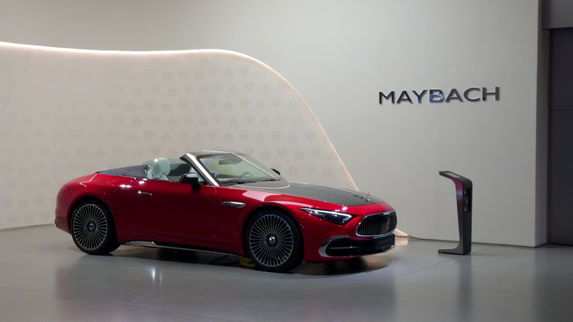 A red Mercedes-Benz SL convertible under a Maybach sign in a white showroom