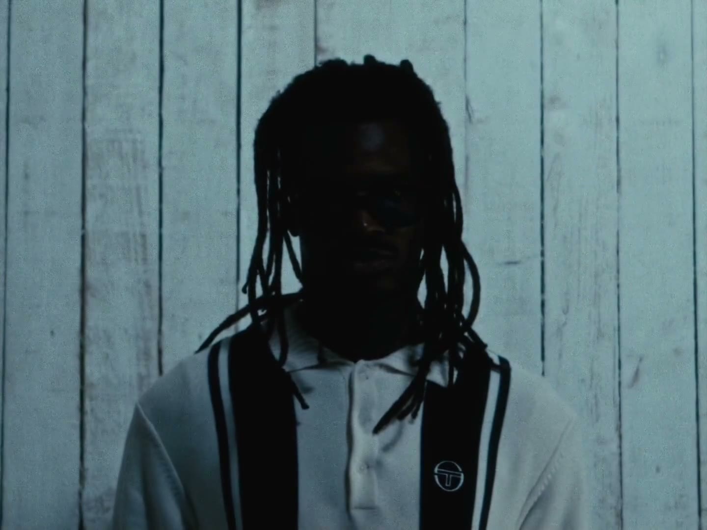 A man with locs in a striped polo against a white timber wall